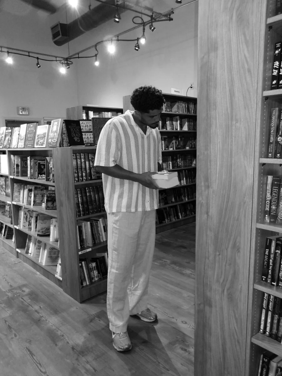 Eddy reading the back of a book between the shelves of a bookstore, in black and white.